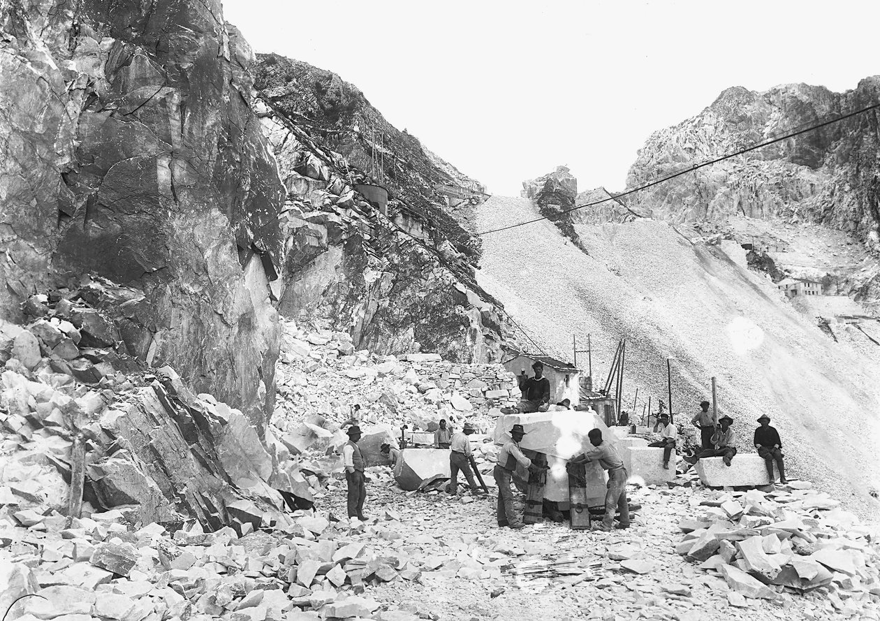 Scavatori al lavoro in una cava di marmo nelle Alpi Apuane, Toscana. Alcuni di loro sono seduti su blocchi di marmo già squadrati da A. Corsini
