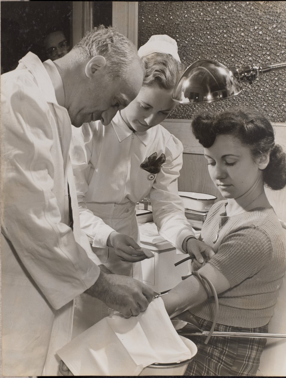[Medico e infermiera inseriscono un ago nel braccio di una donna]. da Arnold Eagle