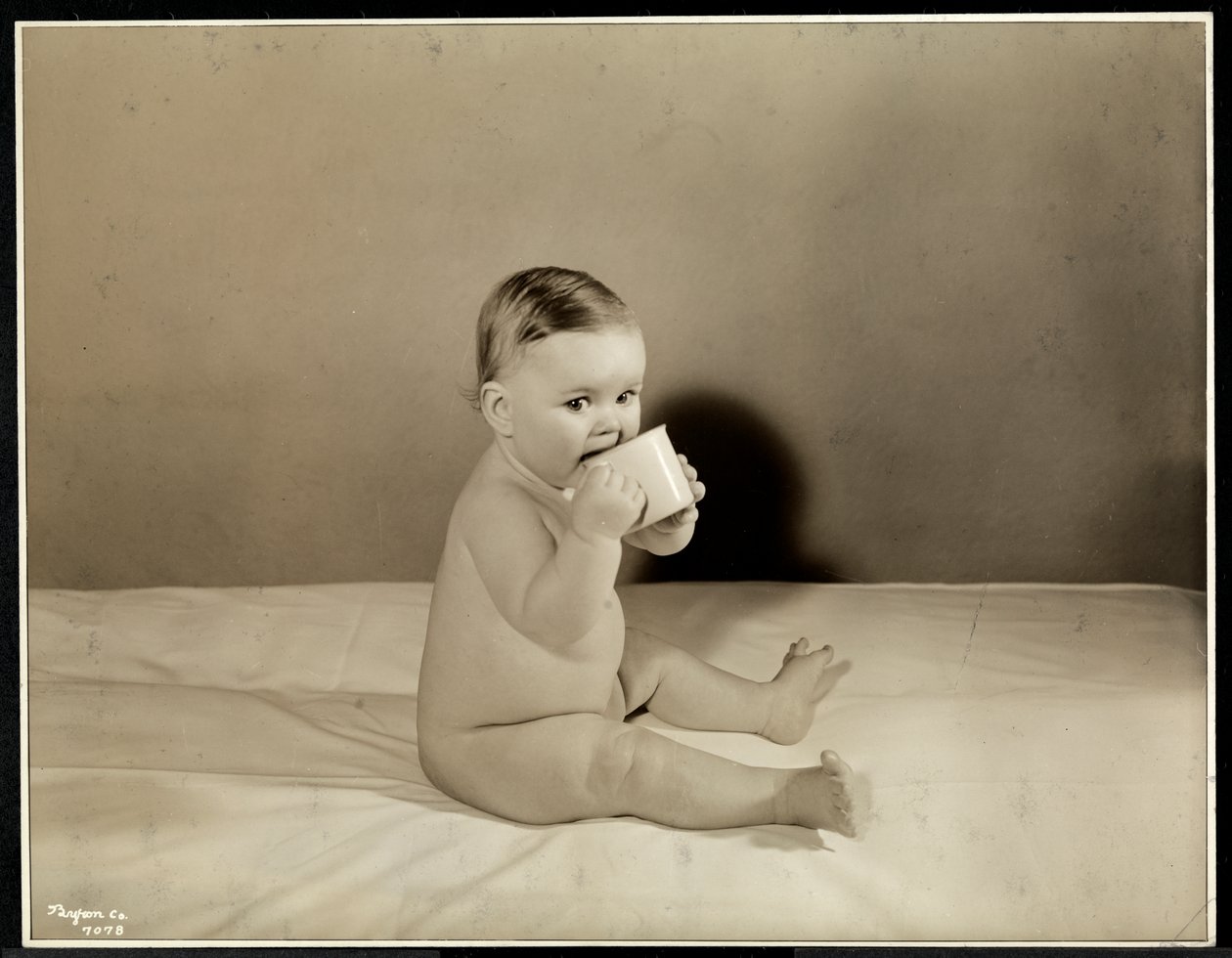 Un bambino seduto a letto che beve da una tazza al Maternity Center Association, New York (1935) da Byron Company