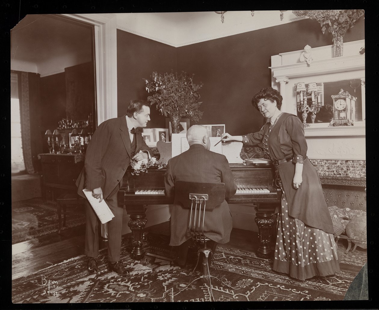Clara De Regand che indica uno spartito mentre un uomo suona il pianoforte, 1910 da Byron Company