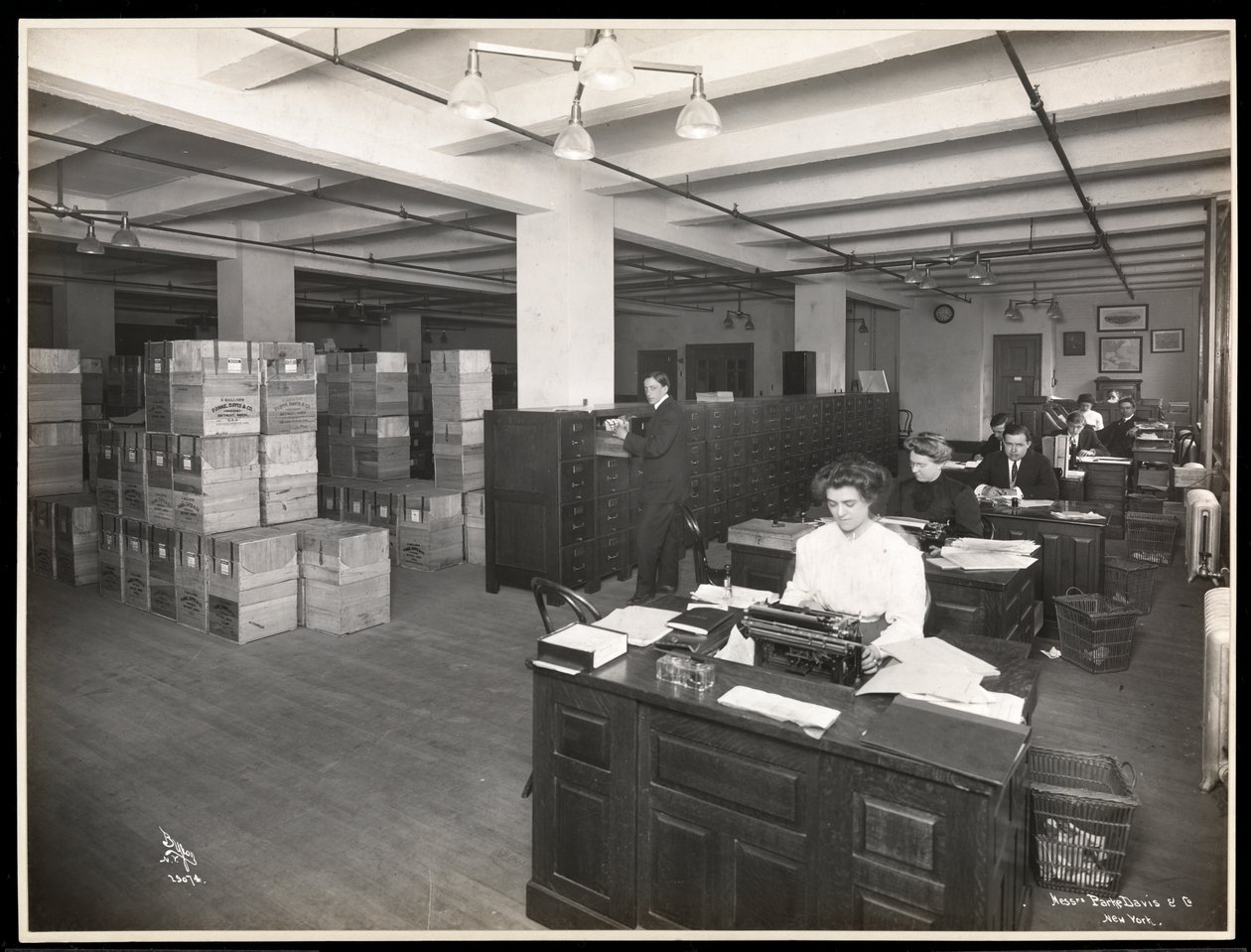 Vista di uomini e donne a scrivanie in quella che sembra essere una sala di spedizione presso Parke, Davis e Co., chimici, Hudson e Vestry Streets, New York, 1910 da Byron Company