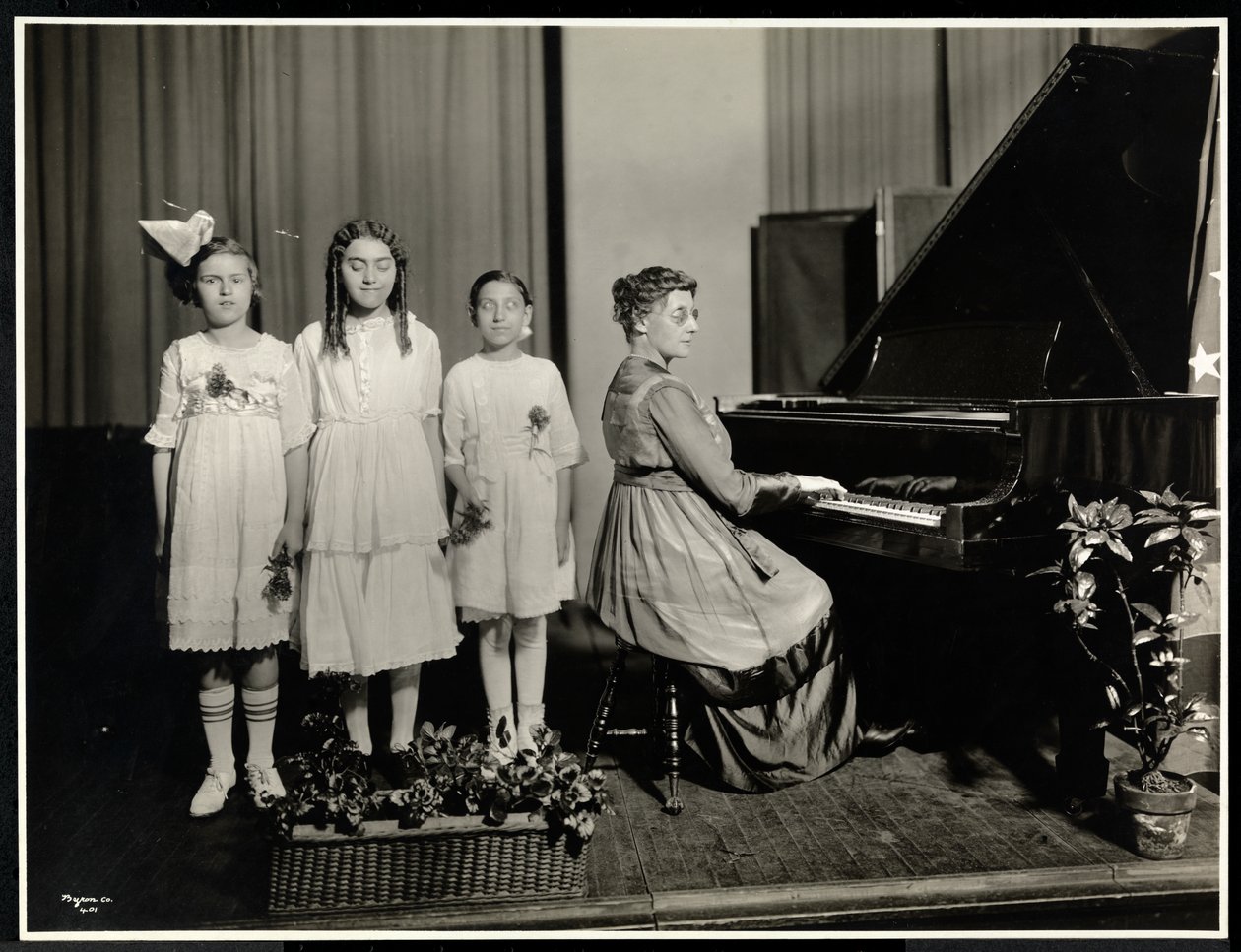 Donna che suona il piano mentre tre ragazze cantano all