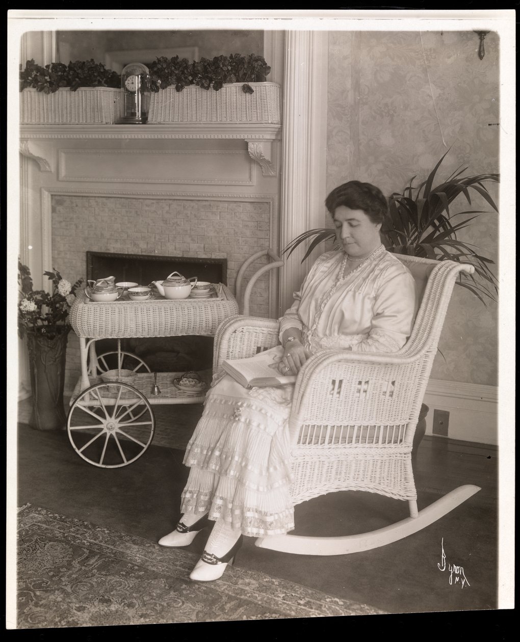 La signora Howard seduta con un libro su una sedia a dondolo nella sua casa al 200, 5th Avenue, New York, 1915-6 da Byron Company