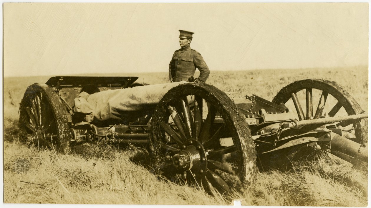 Fotografia orizzontale seppia che mostra un uomo in uniforme accanto a un cannone su ruote in un campo aperto da Carl Michel