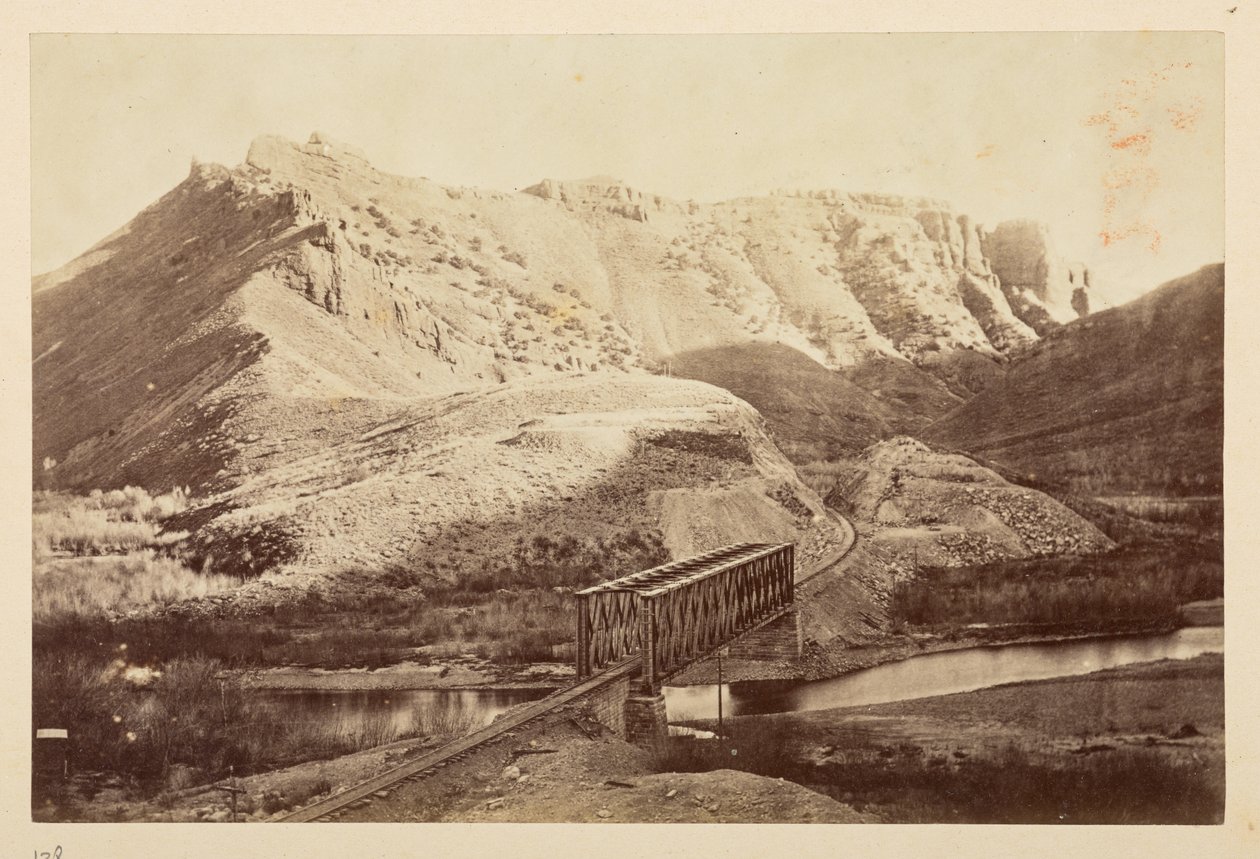 Vedute sulla ferrovia del Pacifico, binario ferroviario che attraversa un fiume su un ponte a travi, con montagne sullo sfondo da English Photographer