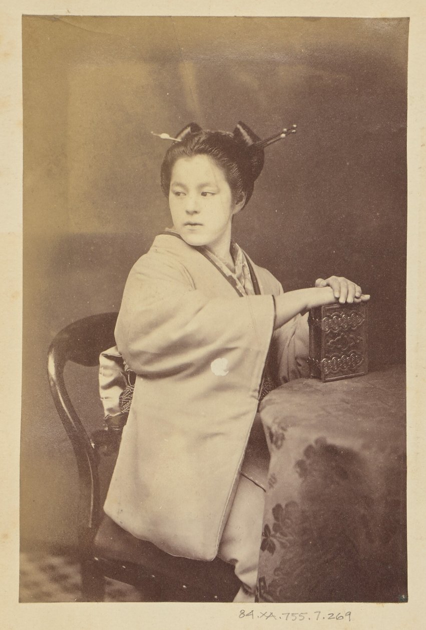 [Donna giapponese seduta con in mano un album di cartes-de-visite a un tavolo]. da Felice Beato