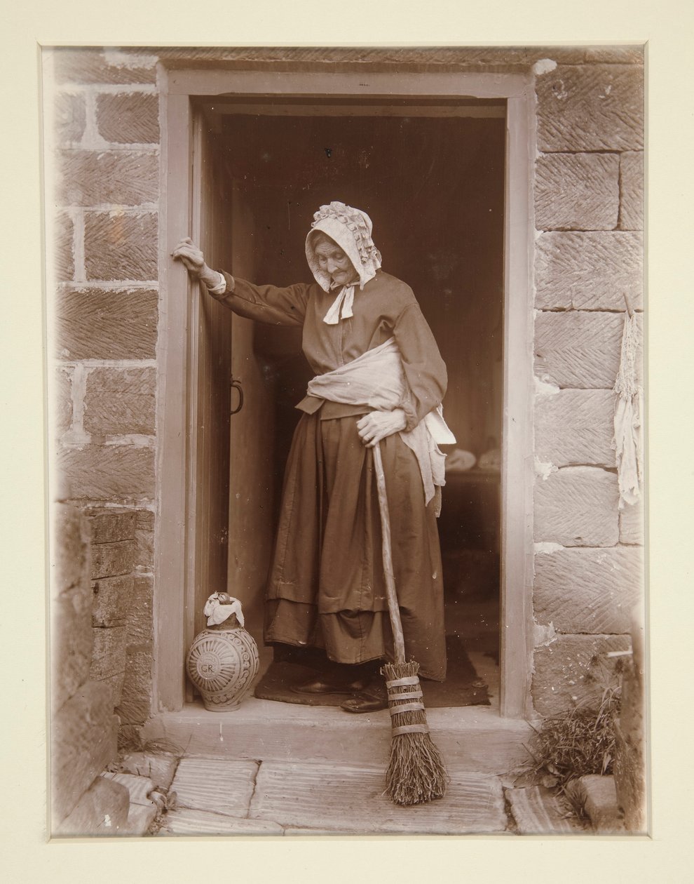 Una vecchia con una bottiglia di lievito alla porta di un cottage da Frank Meadow Sutcliffe