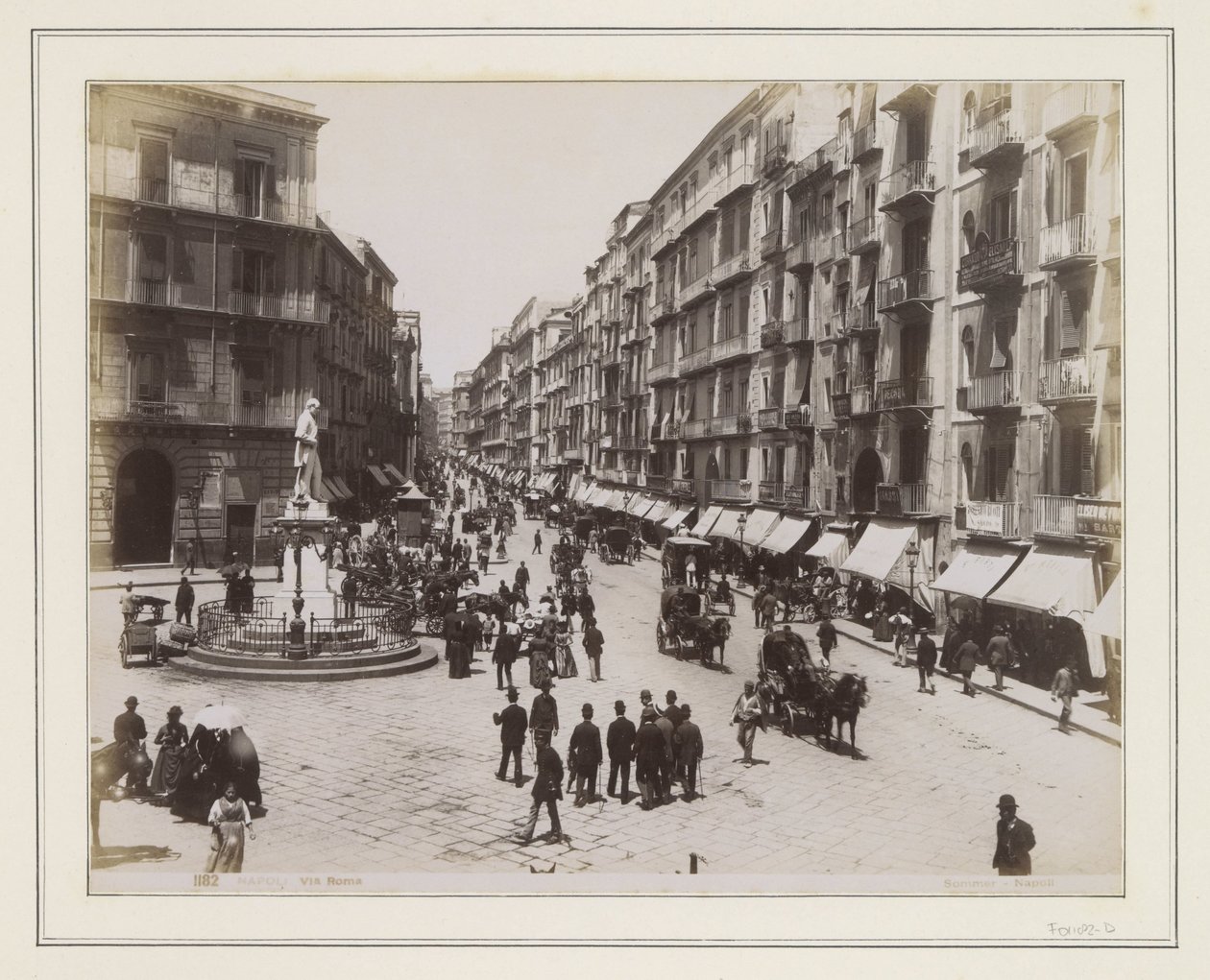 Vista della Via Roma a Napoli con una statua, negozi, carrozze trainate da cavalli e passanti da Giorgio Sommer