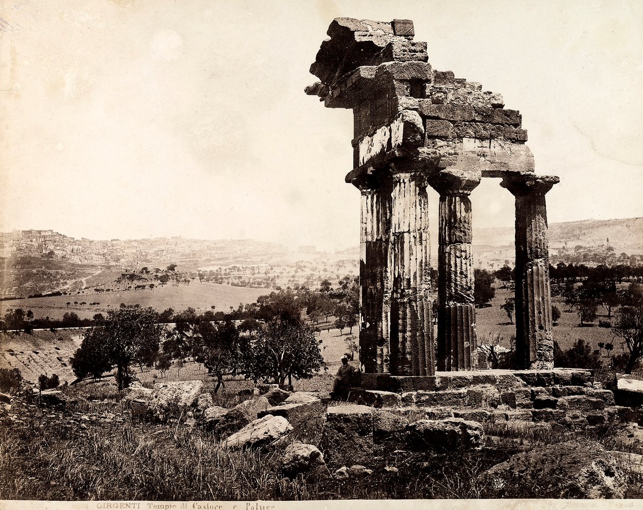 Vista delle quattro colonne rimanenti che sostengono un architrave del Tempio di Castore e Polluce nella Valle dei Templi, Agrigento. Un panorama della città è visibile sullo sfondo da Giorgio Sommer