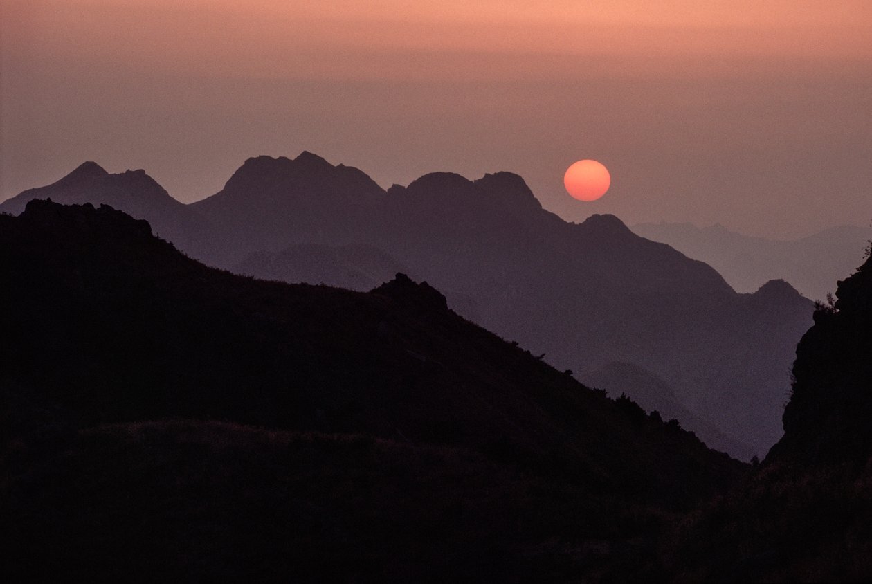 Un sole brillante color cremisi e arancione tramonta sulla catena montuosa di Yan Shan da James L Stanfield