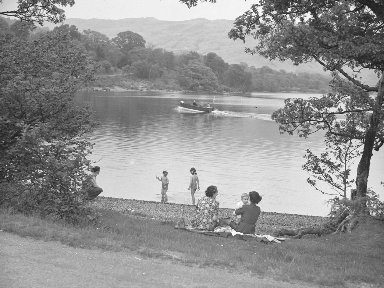 Una famiglia si diverte vicino a un lago, barca sul lago, montagne sullo sfondo da Joseph Hardman
