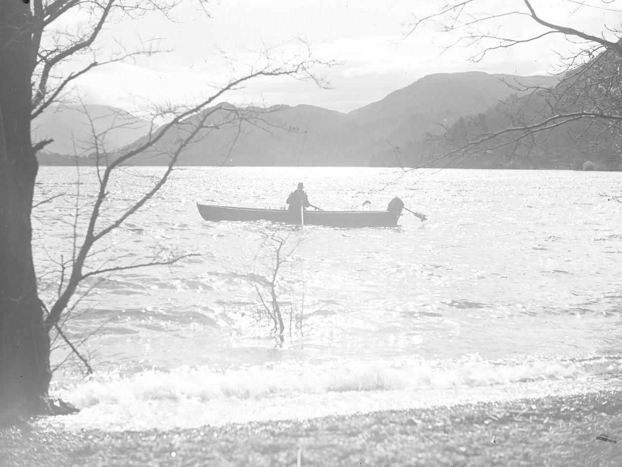 Un uomo seduto in barca su un lago a pescare, con le montagne sullo sfondo da Joseph Hardman