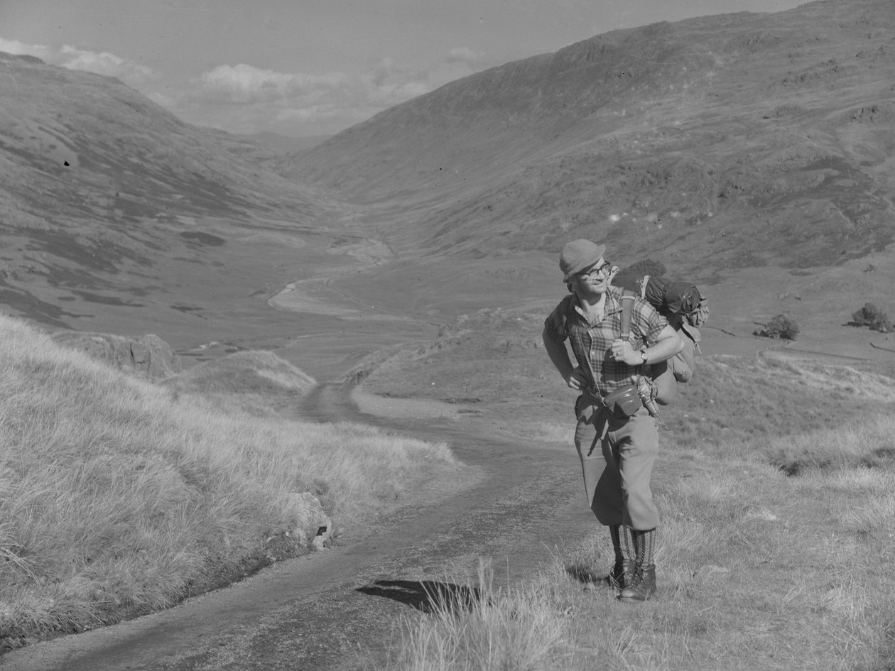 Un uomo che cammina con uno zaino sulle spalle in un paesaggio aperto della valle da Joseph Hardman