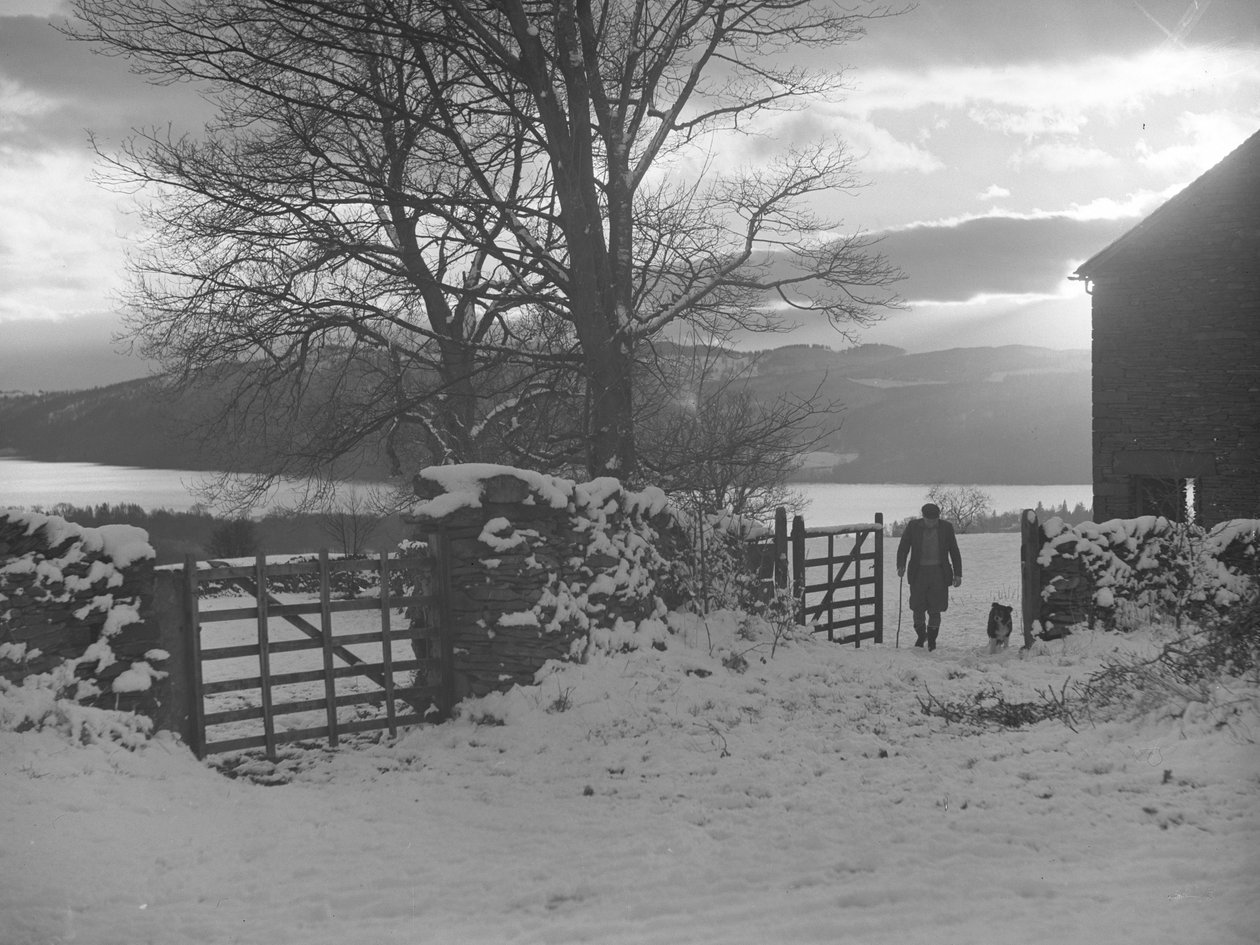 Uomo e cane che attraversano il cancello verso la telecamera nella neve con Thirlmere alle spalle da Joseph Hardman