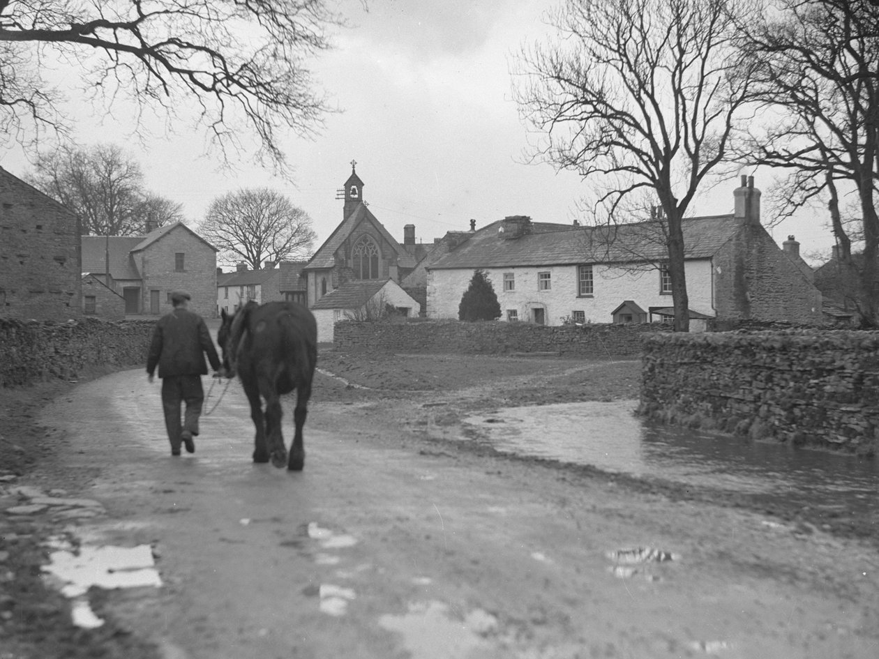 Uomo che conduce il cavallo lungo la strada, lontano dalla telecamera, verso gli edifici del villaggio e la chiesa; architettura; religioso; ecclesiastico; da Joseph Hardman