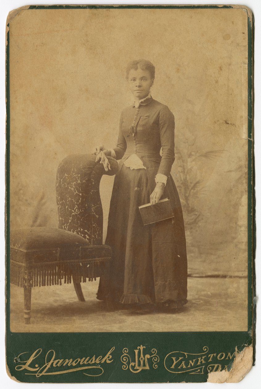 Fotografia di una donna in piedi accanto a una sedia e che tiene un libro, fine XIX secolo da Louis Janousek