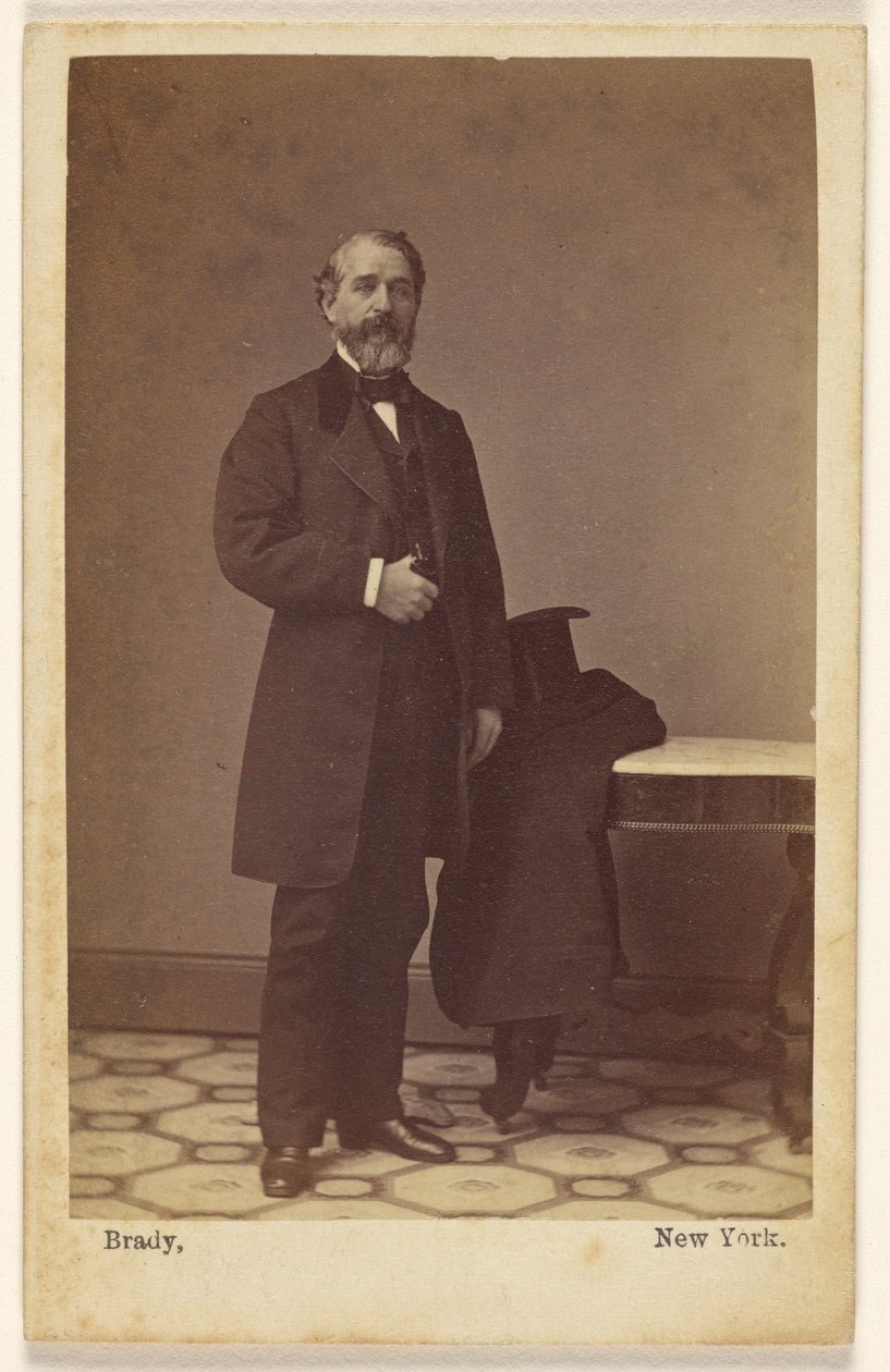 [Uomo barbuto non identificato in piedi; un cappello a cilindro e un cappotto sul tavolo lì vicino] da Mathew B. Brady