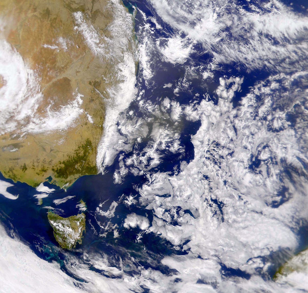 Fotografia satellitare del Mar di Tasman parzialmente coperto da nuvole. A sinistra parte dell