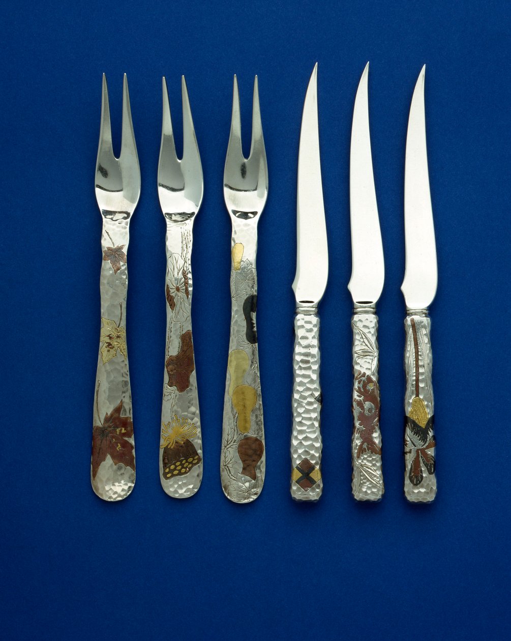 Parte di un set fine e raro di 36 coltelli e forchette da dessert, i manici martellati a punti intarsiati con rame patinato e oro variegato, con dettagli incisi di vari disegni floreali, animali e geometrici, c.1880 da Tiffany and Company