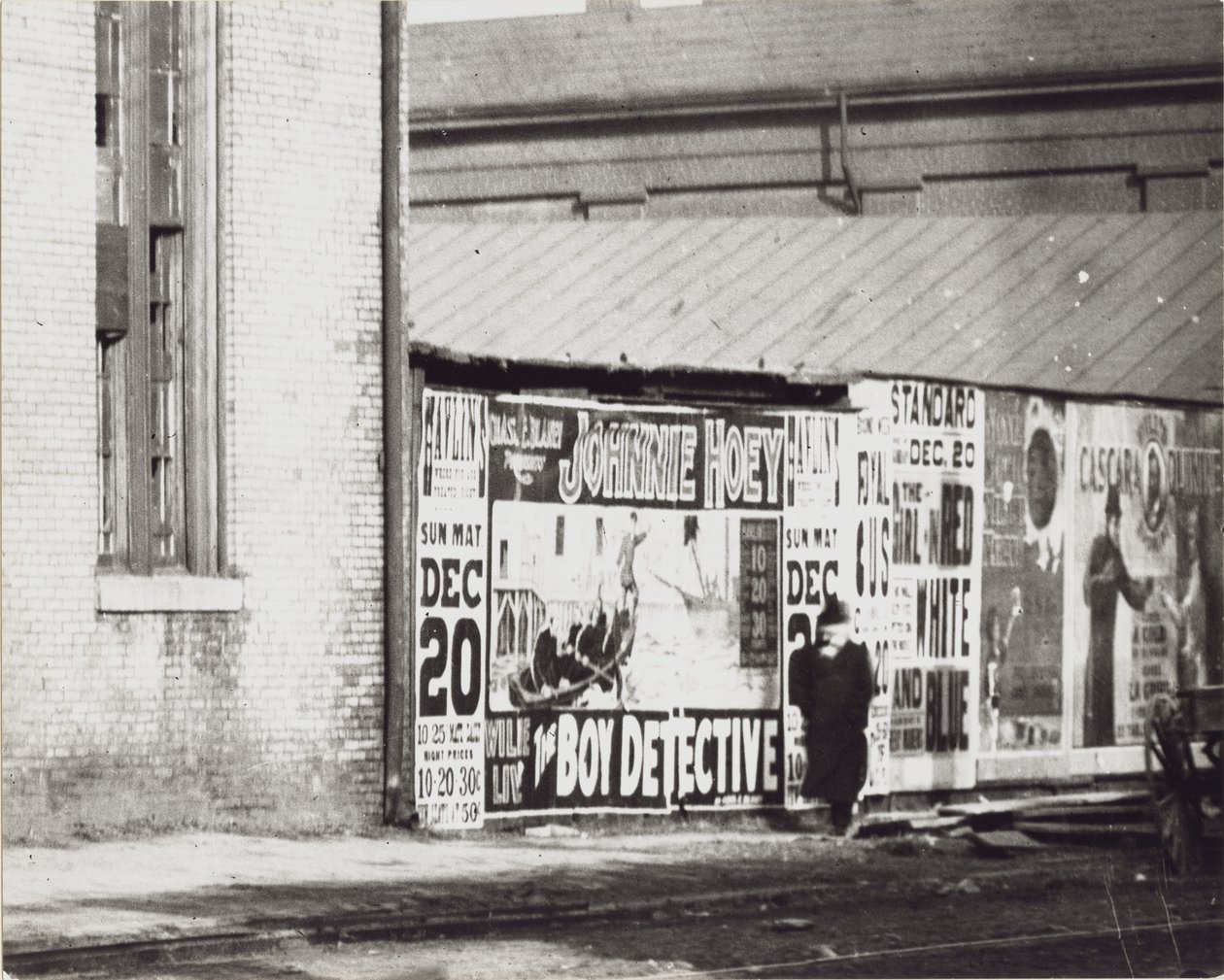 Un uomo passa davanti a un muro di manifesti pubblicitari, incluso uno per Johnnie Hoey The Boy Detective al Havlin