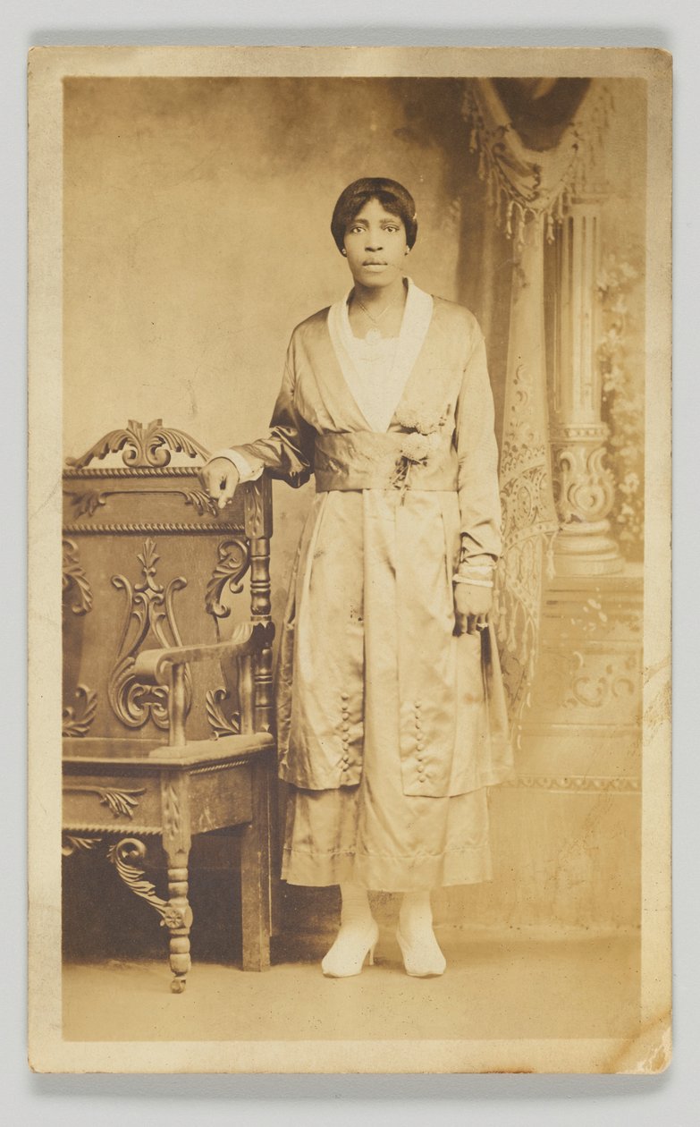 Cartolina fotografica di una donna accanto a una sedia di legno, 1904-1918 da Unbekannt
