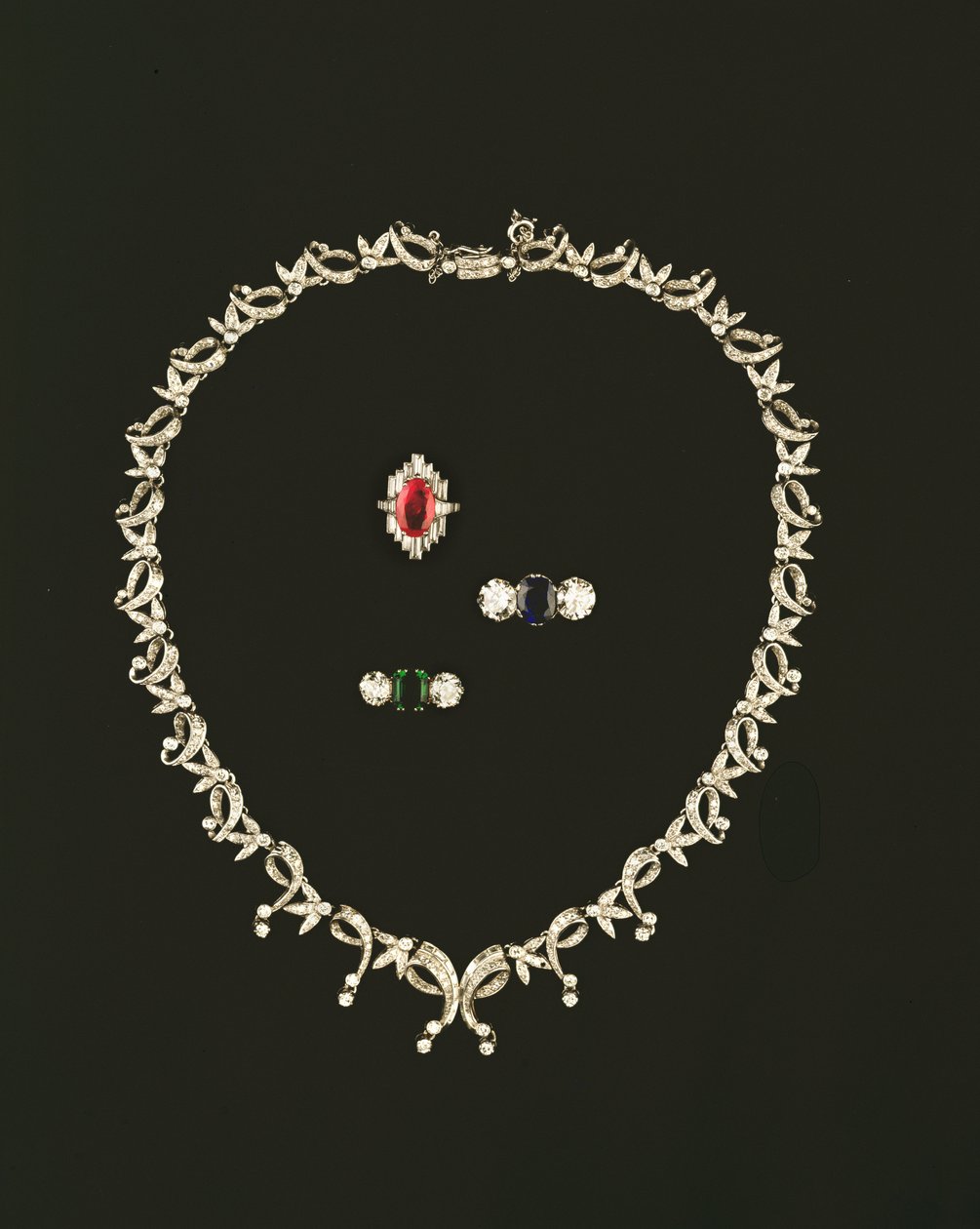 Collana a rotolo e foglia Art Deco; anello a grappolo in rubini e diamanti; anello a tre pietre in zaffiro e diamanti; anello a tre pietre in smeraldo e diamanti da Unbekannt Unbekannt