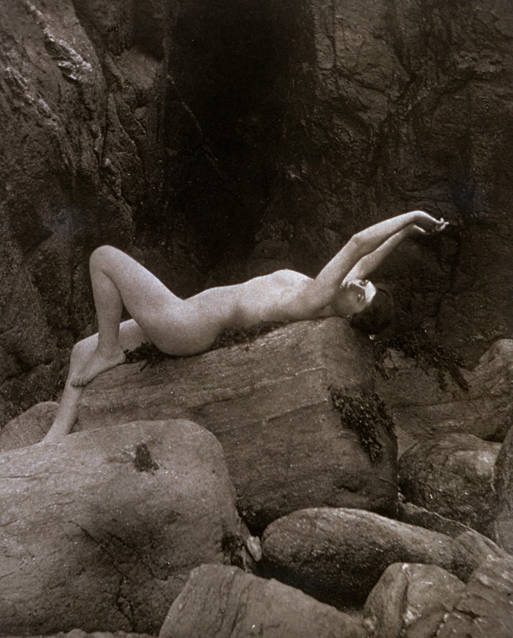 Una giovane donna nuda in posa artistica reclinata su una roccia da Unbekannter Künstler