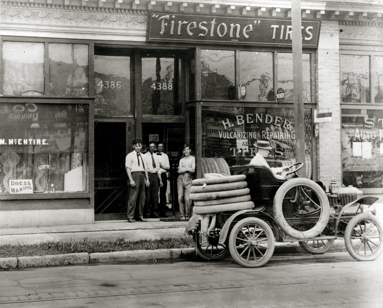Uomini e camion per la riparazione di pneumatici automobilistici radunati fuori dalla concessionaria H. Bender Firestone Tire in 4388 Olive Street da Unknown