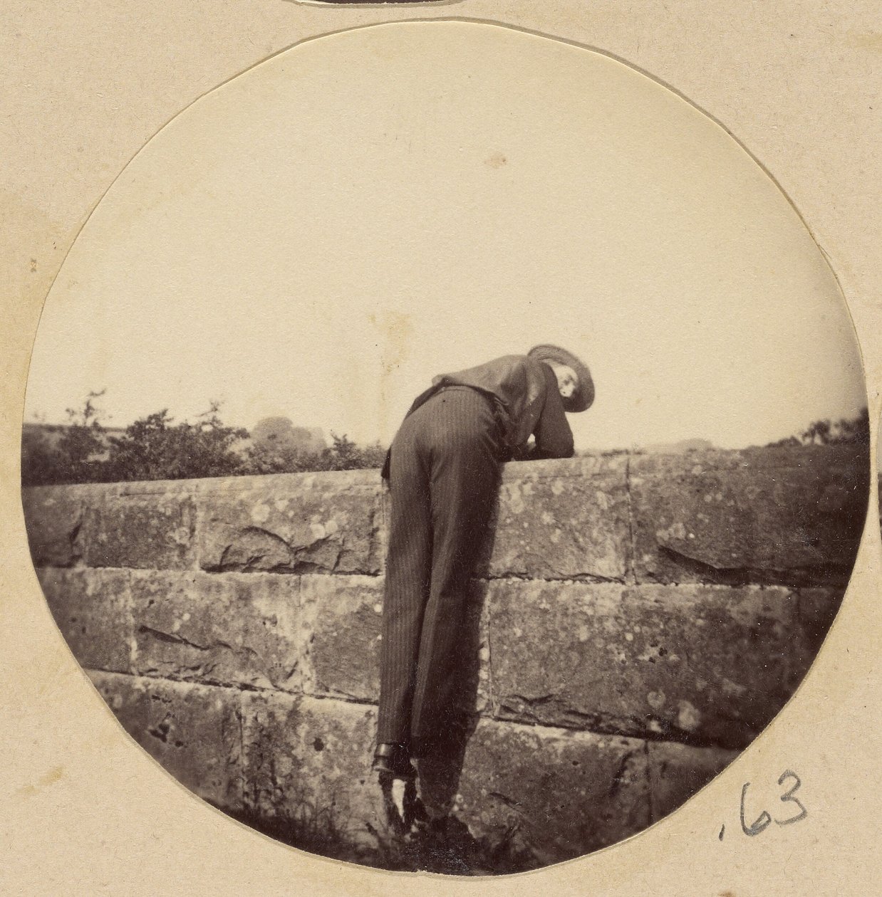 [Uomo con il cappello piegato su un muro di pietra] da Unknown artist