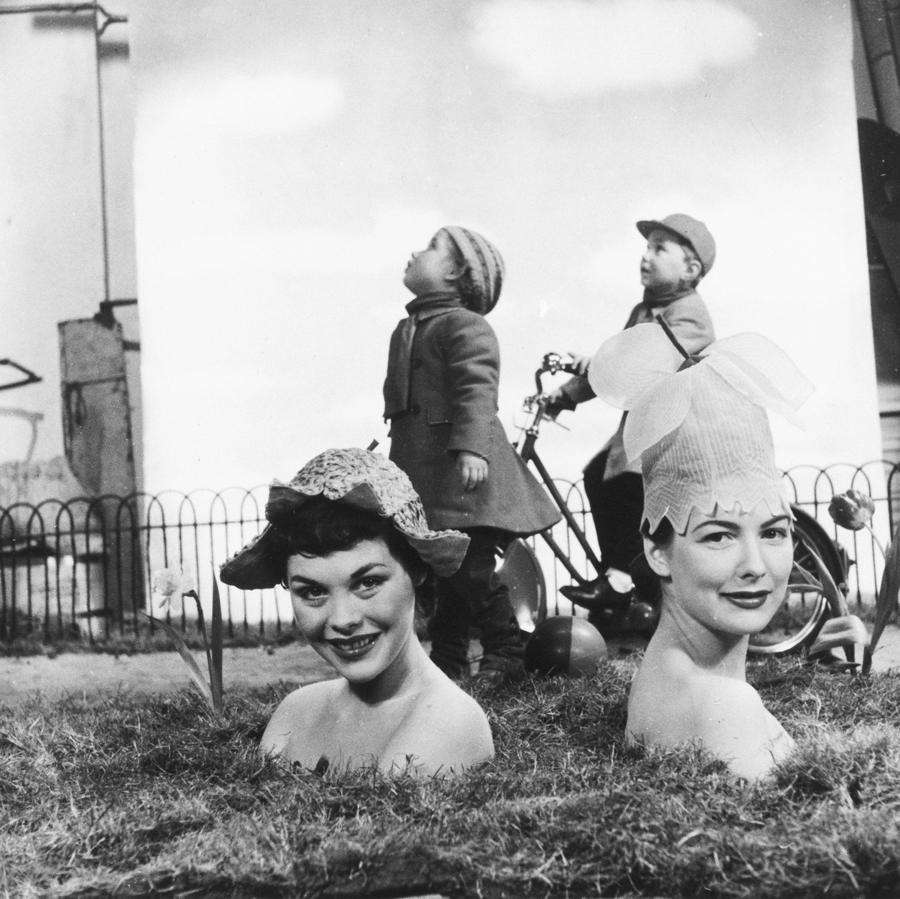 Donne che indossano cappelli a forma di fiore, con il corpo nascosto nel terreno, dando l
