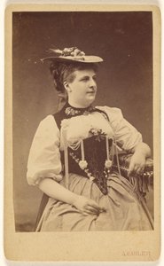 [Donna non identificata in costume indigeno con cappello, seduta].