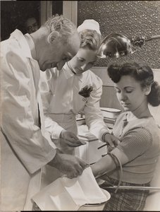 [Medico e infermiera inseriscono un ago nel braccio di una donna]. da Arnold Eagle