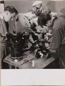 [Cinque giovani lavorano intorno a un banco di lavoro]