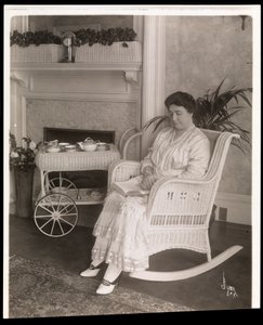 La signora Howard seduta con un libro su una sedia a dondolo nella sua casa al 200, 5th Avenue, New York, 1915-6