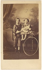 [Bambino non identificato in piedi accanto a una bambina non identificata seduta su un tavolo, un grande cerchio appoggiato su una gamba del tavolo].