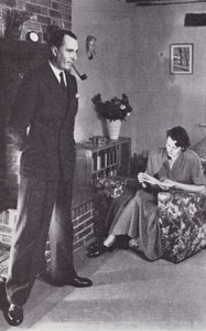 La moglie legge, mentre il marito si scalda la schiena contro il fuoco, c.1950 da English Photographer