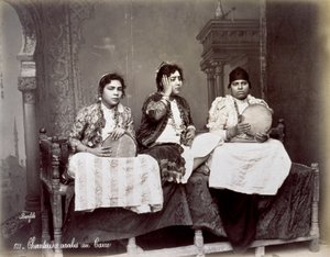 Ritratto di tre giovani cantanti arabi in abiti etnici con lunghe collane. Posano in studio, seduti. Due di loro tengono un tamburello