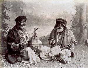 Ritratto di due musicisti arabi in abiti etnici umili. Gli uomini anziani posano in studio, seduti a terra. Dietro di loro c