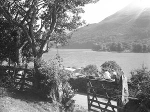 Quattro persone sedute su un muretto a secco a fare un picnic con vista sul lago, auto parcheggiata con il bagagliaio aperto