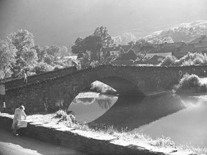 Donna seduta sul muro che studia una mappa con fiume e ponte di pietra sullo sfondo