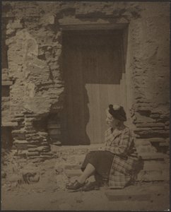 [Donna seduta davanti a un edificio in rovina]