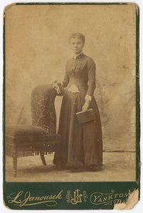 Fotografia di una donna in piedi accanto a una sedia e che tiene un libro, fine XIX secolo da Louis Janousek