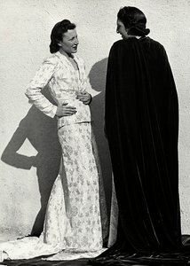 Due modelle presentano creazioni della casa di moda italiana "Dragoni". Una modella indossa un abito in tessuto operato composto da giacca e lunga gonna con strascico. L
