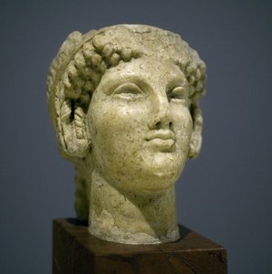Testa di ragazza (Kore), scultura del periodo ellenistico romano (III-II secolo d.C.), volto molto espressivo, zigomi prominenti a est, sorriso, capelli ricci, stile arcaico di Ionia nel VI secolo a.C. che si perpetuò a lungo da Roman