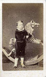 Ragazzo giovane in piedi accanto a un cavallo a dondolo da Silas Eastham