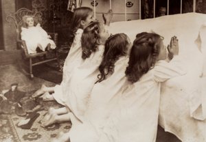 Quattro bambine inginocchiate accanto a un letto mentre recitano la preghiera serale