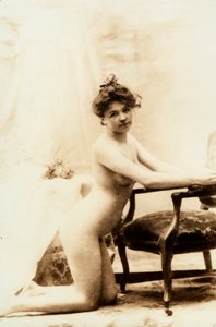 Ritratto nudo di una giovane donna inginocchiata davanti a una piccola poltrona.