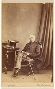 [Uomo non identificato dai capelli bianchi seduto, con bastone, cappello a cilindro e libro sul tavolo a sinistra]. da W. and D. Downey