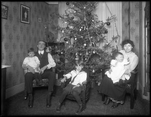 Ritratto di gruppo informale di una famiglia non identificata nel loro appartamento seduti davanti a un albero di Natale, New York City, c.1915-16
