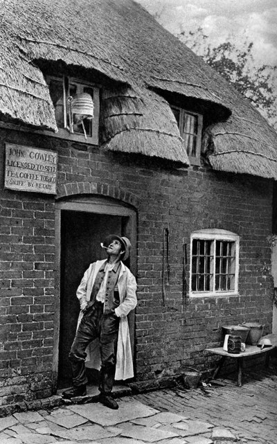 Un uomo che fuma una pipa fuori da un negozio, Worcestershire, c1922 da A. W. Cutler